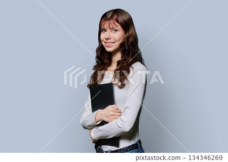 Portrait of beautiful girl teenage student holding laptop on gray background 134346269