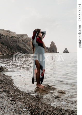 Woman Beach Coastline - A woman stands on a rocky beach by the ocean, looking out at the water. The sky is cloudy and the water is calm. Woman Beach Coastline - A woman stands on a rocky beach by the ocean, looking out at the water. The sky is cloudy and the water is calm. 134346271