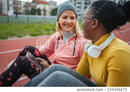 Diverse women friends resting and talking on running track 134346873