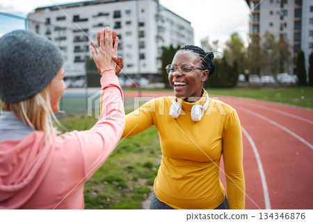 Women high-fiving on running track celebrating success Women high-fiving on running track celebrating success 134346876