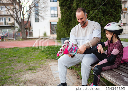 Father helping daughter put on inline skates in park 134346895
