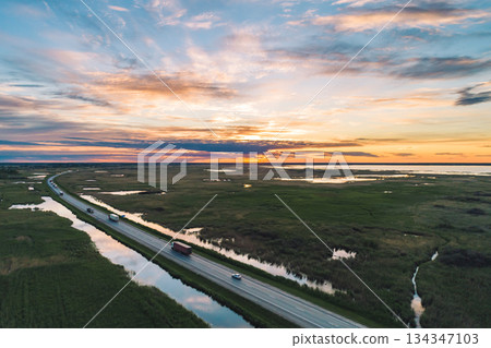 Vehicles travel along a highway through the green countryside at sunset 134347103