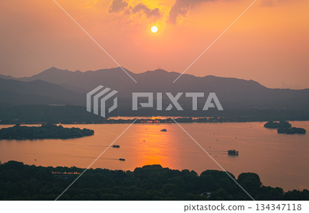 Aerial view of an orange sunset over West Lake and Hangzhou city with distant mountain. Aerial view of an orange sunset over West Lake and Hangzhou city with distant mountain. 134347118