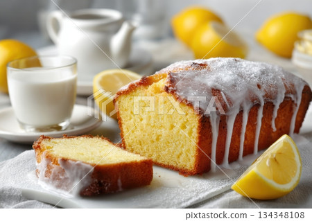 Homemade lemon drizzle cake with icing. Classic lemon pound cake with citrus glaze and zest. Whole loaf, side view, close up. Fresh homemade baked dessert with lemon slices. Blurred tea set background 134348108