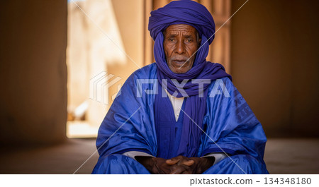 In a quiet space, a man from Mauritania sits calmly, stroking his beard as he listens closely to something. The light and shadows create a warm atmosphere around him. In a quiet space, a man from Mauritania sits calmly, stroking his beard as he listens closely to something. The light and shadows create a warm atmosphere around him. 134348180
