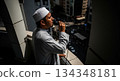 A muezzin stands at a high point, using a microphone to deliver the adhan. Below, city streets are busy as people move about, engaging in daily activities. 134348181
