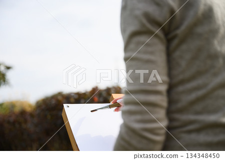 Close-up of artist painting on blank canvas outdoors. 134348450