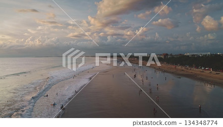Dreamland Beach in Bali, Indonesia, showcases a stunning sunset scene with tourists along the shoreline, gentle waves, and a peaceful, cloudy sky 134348774