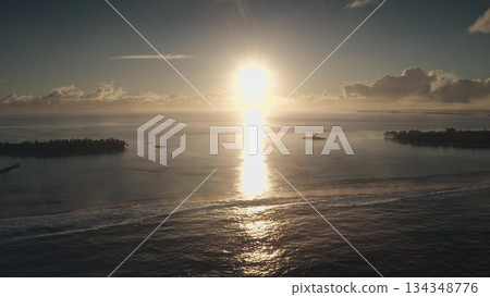 Golden sunlight gracefully illuminates the ocean surface, creating shimmering reflections. Distant islands silhouette against the horizon, casting serene vibes at dusk. 134348776