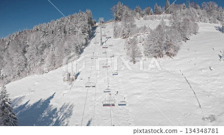 Chairlift ascending a snowy mountain slope on bright, sunny winter day, stunning views of snow covered trees and ski slopes stretching below. Bukovel ski resort. Winter wild nature travel background Chairlift ascending a snowy mountain slope on bright, sunny winter day, stunning views of snow covered trees and ski slopes stretching below. Bukovel ski resort. Winter wild nature travel background 134348781
