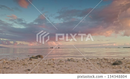 Moorea island beach seeing calm waves and people swimming in the ocean under a beautiful twilight sky with pink and purple clouds reflecting on the water surface Moorea island beach seeing calm waves and people swimming in the ocean under a beautiful twilight sky with pink and purple clouds reflecting on the water surface 134348804