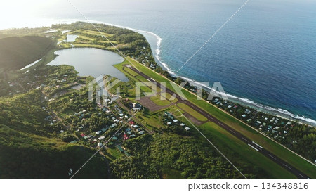 Moorea airport runway extending along the vibrant green coastline of the tropical island, showcasing the deep blue ocean, lush vegetation, and local settlements from an aerial drone perspective Moorea airport runway extending along the vibrant green coastline of the tropical island, showcasing the deep blue ocean, lush vegetation, and local settlements from an aerial drone perspective 134348816