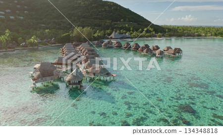 Luxurious resort bungalows extending into the crystal-clear turquoise lagoon of Moorea, French Polynesia, offering an idyllic escape surrounded by lush green mountains and a vibrant coral reef Luxurious resort bungalows extending into the crystal-clear turquoise lagoon of Moorea, French Polynesia, offering an idyllic escape surrounded by lush green mountains and a vibrant coral reef 134348818