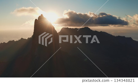 Moorea island majestic mountain peaks emerging from the dark silhouette as golden sunbeams radiate across the sky, highlighting the tranquil tropical landscape and inspiring a sense of calm 134348821