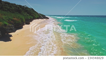 Breathtaking aerial view capturing turquoise ocean waves gently crashing on a pristine sandy beach, surrounded by lush green vegetation on Sumba Island, Indonesia 134348829
