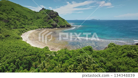 Fiji, Kuata island: secluded tropical beach with crystal clear blue water lagoon lapping against lush greenery mountain hill and a rugged coastline. Drone flight shows wild nature beauty 134348839