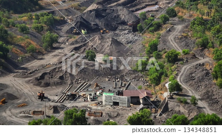 Large scale open pit mining operation showing excavators, dump trucks, and various industrial equipment actively extracting coal from the landscape, forming vast piles of raw material 134348851