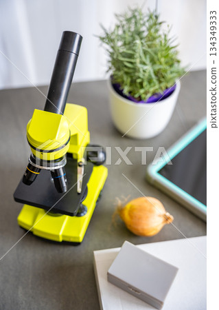 Yellow microscope, tablet, and experiment box on a desk. Educational science kit for kids learning microscopy and biology at home. 134349333