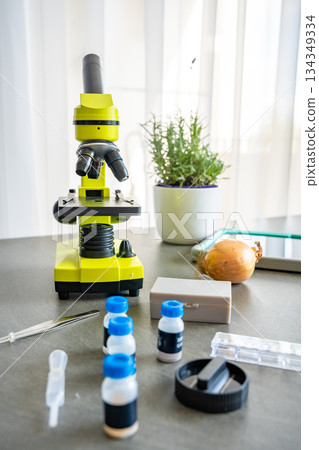 Microscope and science kit with glass slides, tweezers, and prepared chemical samples on a table. Educational tools for kids experiments in biology and chemistry at home. Microscope and science kit with glass slides, tweezers, and prepared chemical samples on a table. Educational tools for kids experiments in biology and chemistry at home. 134349334