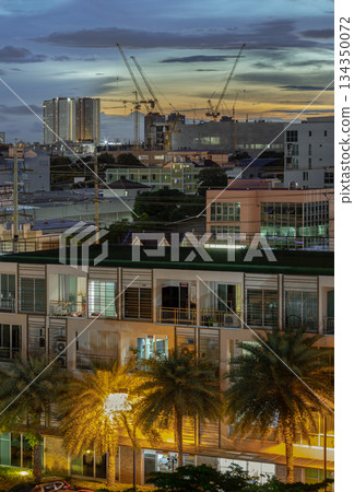 The cityscape sunset features multi-story buildings and construction cranes silhouetted against a bright horizon The cityscape sunset features multi-story buildings and construction cranes silhouetted against a bright horizon 134350072