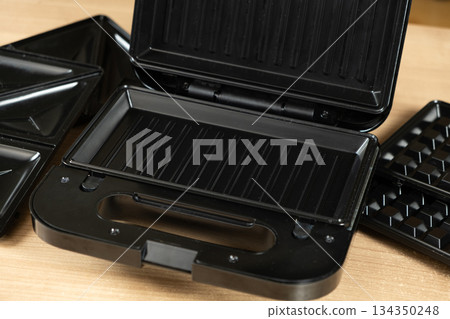 Open Electric Sandwich Maker and Waffle Grill with Interchangeable Plates on a Kitchen Table. Open Electric Sandwich Maker and Waffle Grill with Interchangeable Plates on a Kitchen Table. 134350248