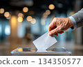 Hand placing paper ballot into transparent voting box 134350577
