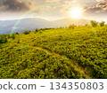 hiking trail through mountain landscape at sunset. mountain range under sky with clouds in evening light. scenery with green grass and rolling hills. timeless nostalgia book cover with rainbow 134350803