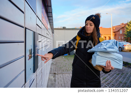 Woman holding packages and pressing keypad on parcel locker outdoors 134351207