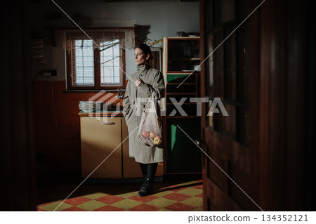 Woman standing in old rural kitchen with half-empty shopping bag. 134352121
