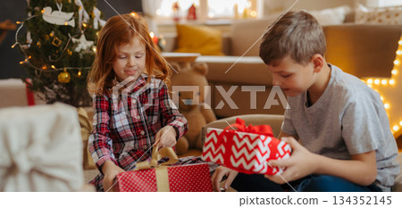 Siblings opening christmas presents in pajamas. Siblings opening christmas presents in pajamas. 134352145