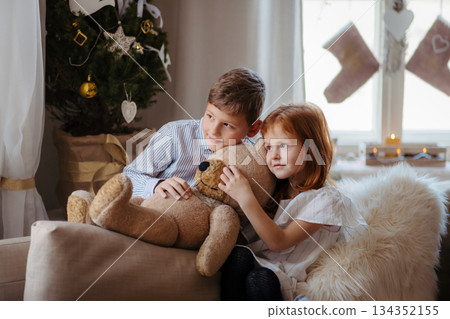 Small girl and boy indoors at home at Christmas, holding teddy bear. Small girl and boy indoors at home at Christmas, holding teddy bear. 134352155