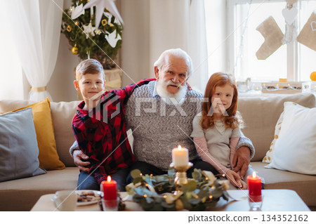 Kids spending Christmas time with senior grandfather indoors at home. Kids spending Christmas time with senior grandfather indoors at home. 134352162