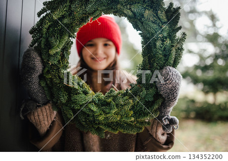 Girl holding a handmade Christmas wreath. Girl holding a handmade Christmas wreath. 134352200