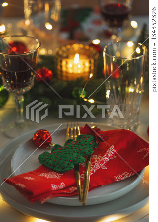 Christmas Table Setting with Red Napkin, Gold Cutlery, Felt Christmas Tree, Festive Decor and Candle Lights Christmas Table Setting with Red Napkin, Gold Cutlery, Felt Christmas Tree, Festive Decor and Candle Lights 134352326