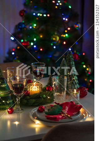 Festive Holiday Table Setting with Christmas Tree, Decorations and Candle Lights against Christmas Tree Festive Holiday Table Setting with Christmas Tree, Decorations and Candle Lights against Christmas Tree 134352327