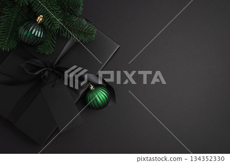 Black Christmas Gift Box with Satin Ribbon and Green Ornaments on Dark Holiday Background Black Christmas Gift Box with Satin Ribbon and Green Ornaments on Dark Holiday Background 134352330