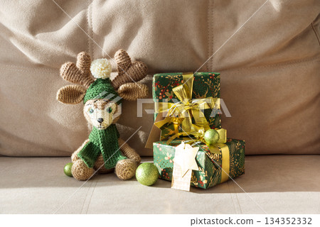 Crocheted Reindeer with Christmas Gift Box and Ornaments on Cozy Holiday Background Crocheted Reindeer with Christmas Gift Box and Ornaments on Cozy Holiday Background 134352332