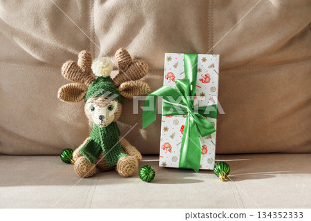 Crocheted Reindeer with Christmas Gift Box and Ornaments on Cozy Holiday Background 134352333