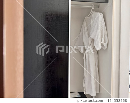 A clean white waffle bathrobe is hanging on a hanger in the hotel closet. High quality photo 134352368