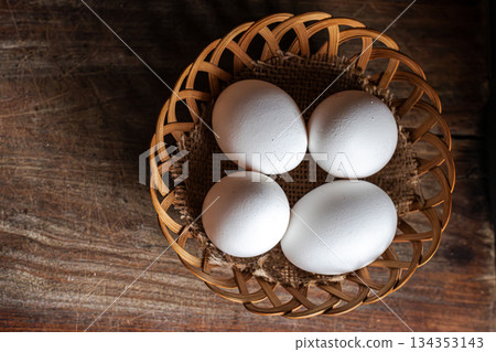 Top view of four white eggs on a woven basket . Wooden background. Copy space 134353143
