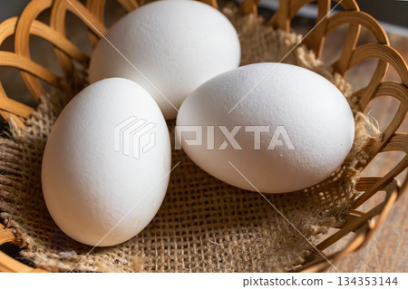 Very close up of three white eggs resting on a rustic basket in soft lighting. Natural light. 134353144