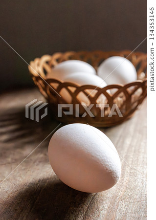 White egg on wooden table with basket of eggs in the blurred background White egg on wooden table with basket of eggs in the blurred background 134353146