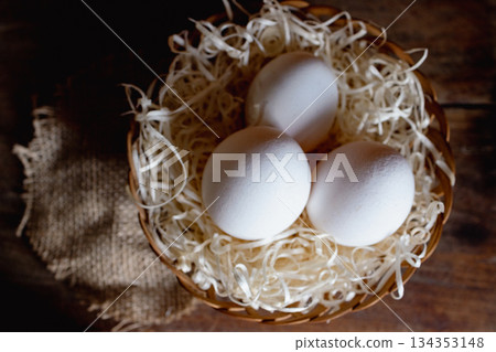 Three fresh white eggs nestled in a rustic basket. Horizontal real image taken from above. 134353148