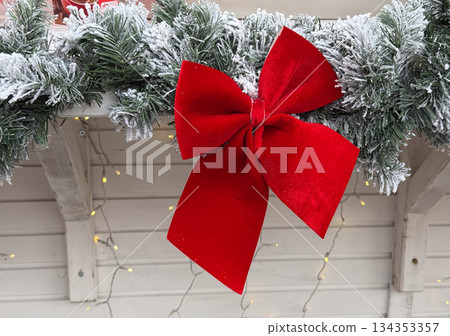 Red velvet bow on frosted pine garland. Christmas decor detail, holiday ornament, winter festive design Red velvet bow on frosted pine garland. Christmas decor detail, holiday ornament, winter festive design 134353357