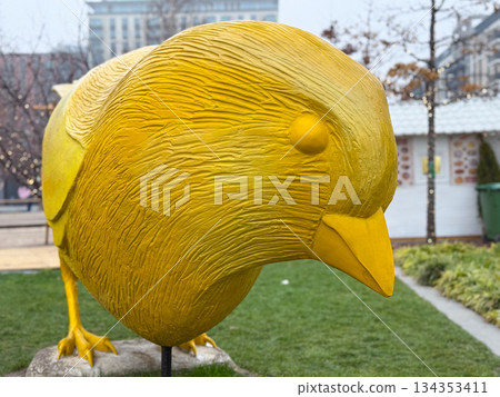 Close up of large yellow bird sculpture in outdoor urban park. Textured surface detail, modern public art, and creative city decor Close up of large yellow bird sculpture in outdoor urban park. Textured surface detail, modern public art, and creative city decor 134353411