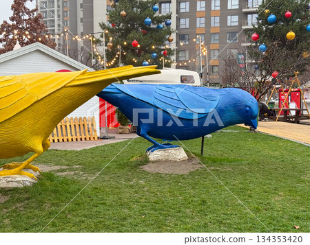 Large colorful bird sculptures displayed on grass at festive urban park. Outdoor art installation, holiday decoration, and public space design 134353420