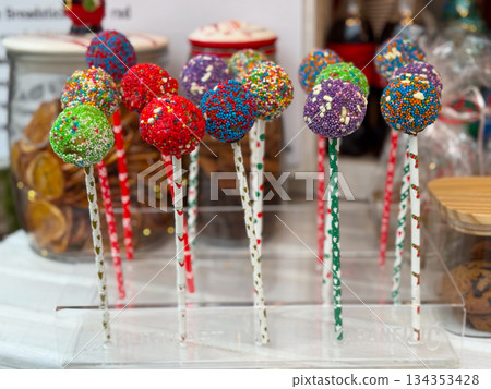 Colorful cake pops covered with sugar sprinkles on sticks. Festive dessert assortment, sweet treats, and holiday confectionery display Colorful cake pops covered with sugar sprinkles on sticks. Festive dessert assortment, sweet treats, and holiday confectionery display 134353428