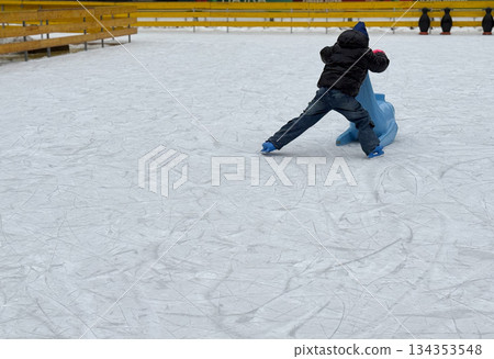 Child pushing a blue skating aid on an empty ice rink. Winter sport learning, independence, and first skating experience Child pushing a blue skating aid on an empty ice rink. Winter sport learning, independence, and first skating experience 134353548