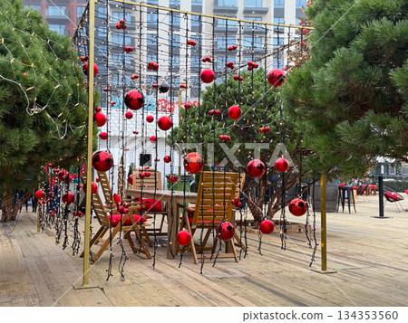 Christmas Outdoor seating area under red ornament light canopy. Festive winter cafe space, holiday decor and cozy seasonal atmosphere Christmas Outdoor seating area under red ornament light canopy. Festive winter cafe space, holiday decor and cozy seasonal atmosphere 134353560