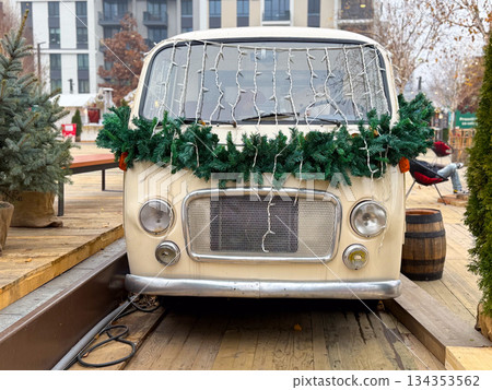Vintage van decorated with Christmas garland and lights at winter market. Festive urban installation, seasonal decor and holiday atmosphere 134353562